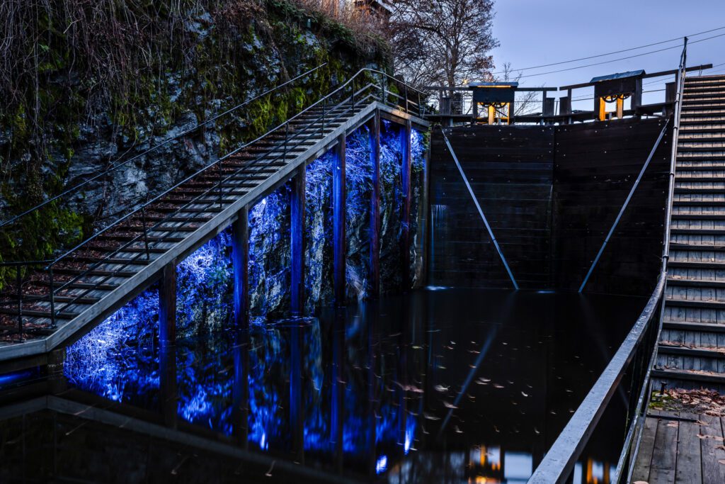 Slusene i Haldenkanalen har fått ny lyssetting. Blå lys på murvegg under trapp opp fra vannet.